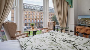 Et hotelværelse med en seng, en stol, et lille bord med en plante og et fjernsyn på en trækommode.