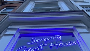 En neonskilte med teksten "Serenity Guest House" på en bygnings facade.