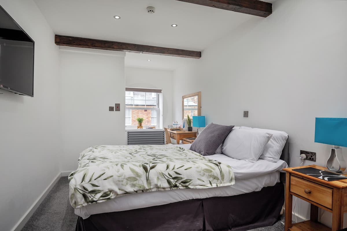 Une chambre à coucher comprenant un lit, une table de chevet, une lampe et un téléviseur fixé au mur.