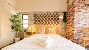A neatly made bed with white linens, a wooden headboard, and a brick wall.