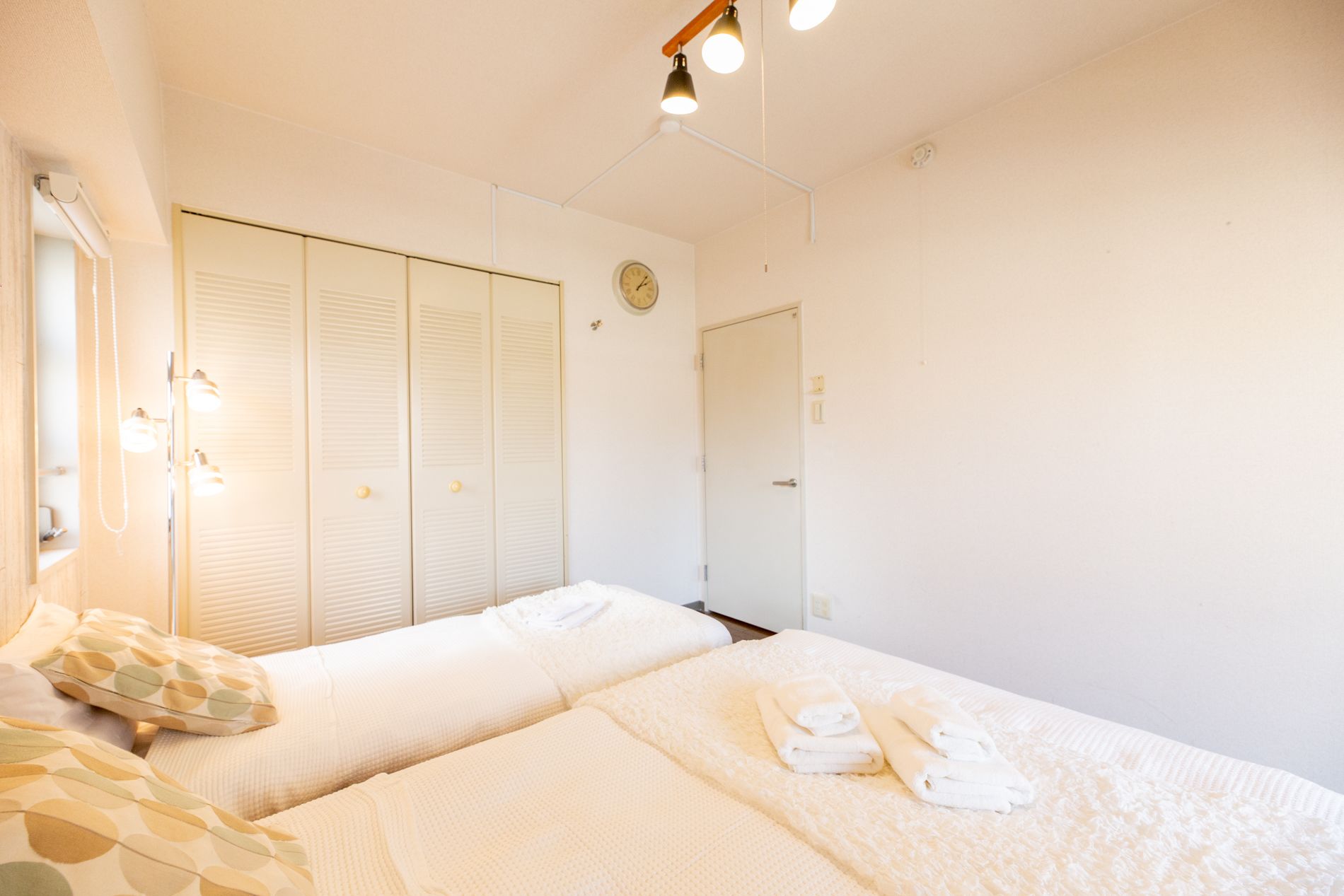 A room with two beds, a wardrobe, a mirror, and a clock on the wall.