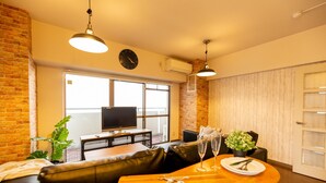 A modern living room with a wooden dining table, leather sofa, and a TV.