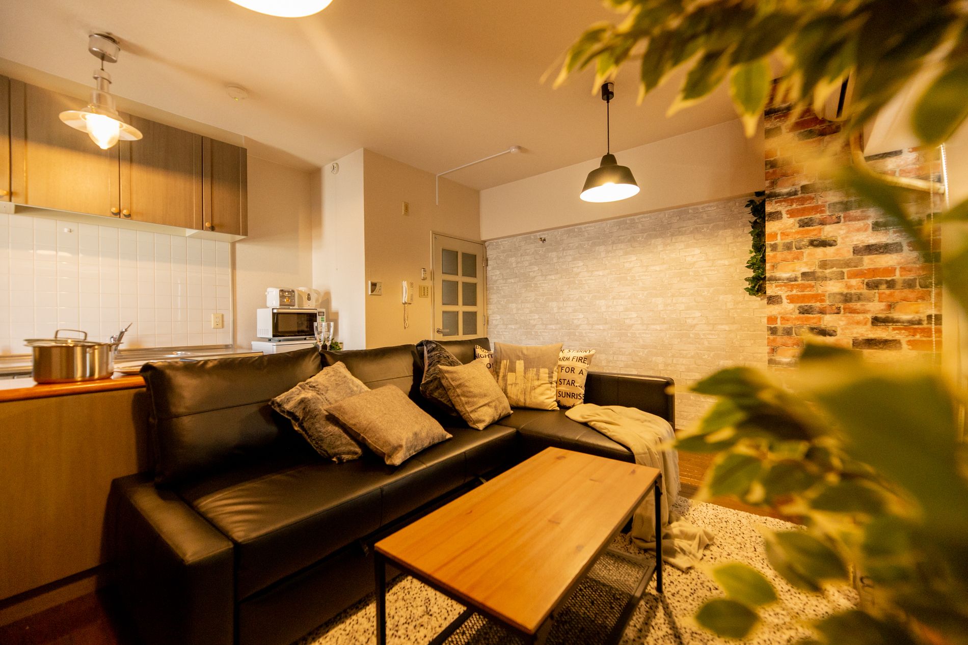 A cozy living room with a black leather sofa, a wooden coffee table, and a brick accent wall.