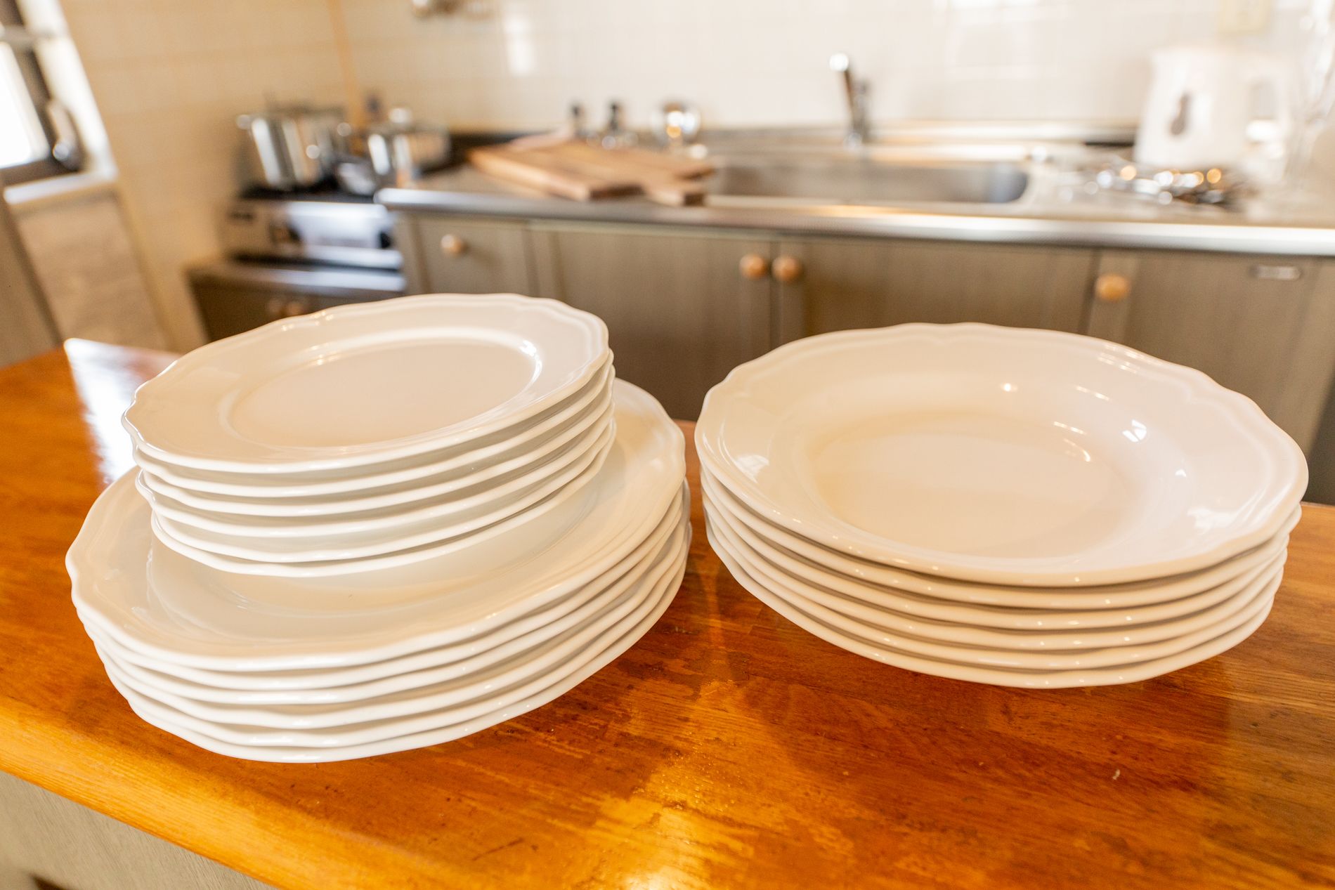 A stack of white plates on a wooden countertop in a kitchen with stainless steel appliances and cabinets.