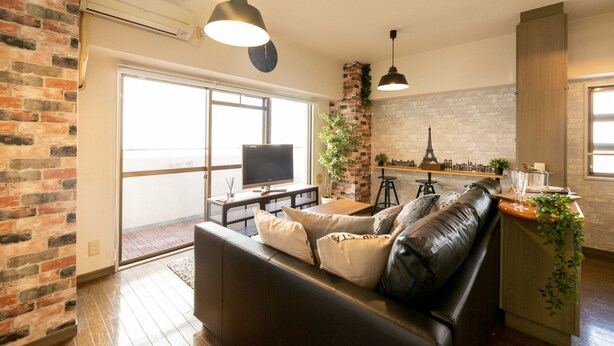 A modern living room with a leather sofa, a flat-screen TV, and a brick accent wall.