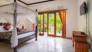 A bedroom with a four-poster bed, a wooden desk, and a sliding glass door leading to a garden.