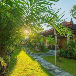 A traditional building with a tiled roof, surrounded by lush greenery and a stone pathway leading to the entrance. - Pondok Wisata Sartaya 2 (Buleleng)