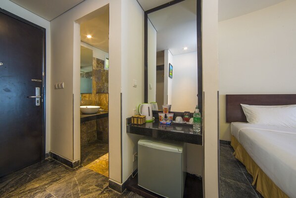 Une chambre d’hôtel équipée d’un lit, d’un petit réfrigérateur, d’un lavabo et d’un miroir.