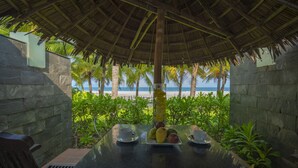 A table with fruit and cups, a thatched roof, stone walls, and a view of the beach. - Temple Da Nang (Da Nang)