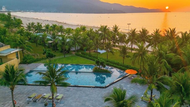 A resort with a swimming pool, palm trees, and a view of the sea at sunset. - Temple Da Nang (Da Nang)
