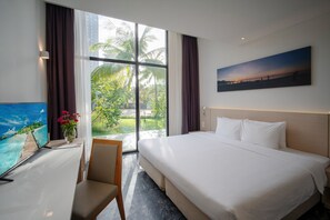 A hotel room with a large bed, a desk with a TV, and a window with a view of palm trees. - Temple Da Nang (Da Nang)