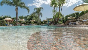 A clear pool with lounge chairs and umbrellas, surrounded by palm trees and a stone wall. - Lovely apartment in Laureana Cilento (SA) with WiFi (Laureana Cilento (SA))