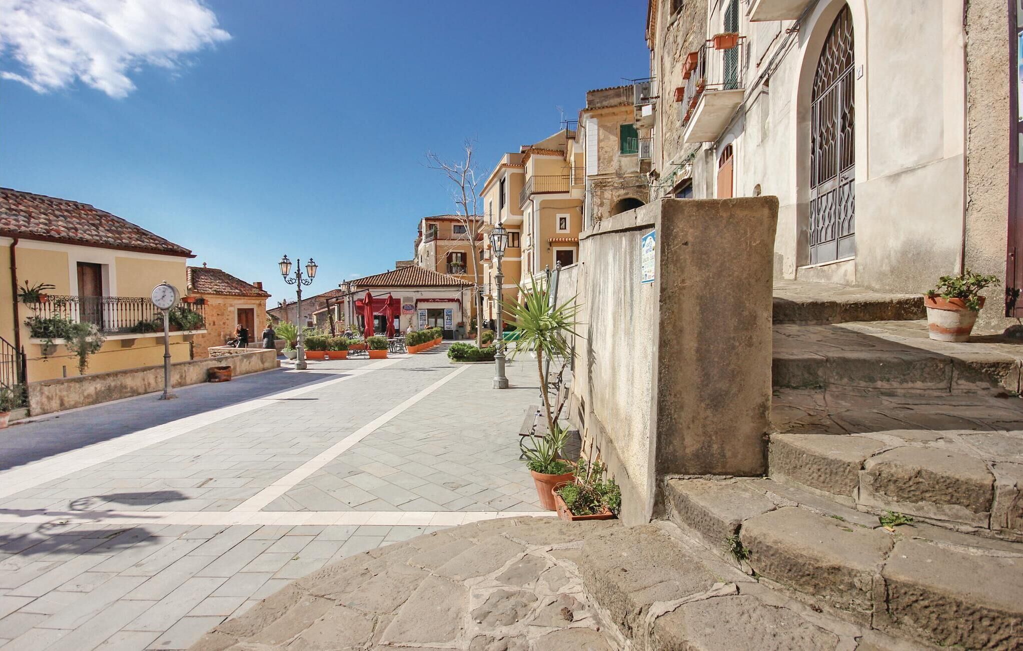 A quiet street with buildings, a clock, and potted plants.