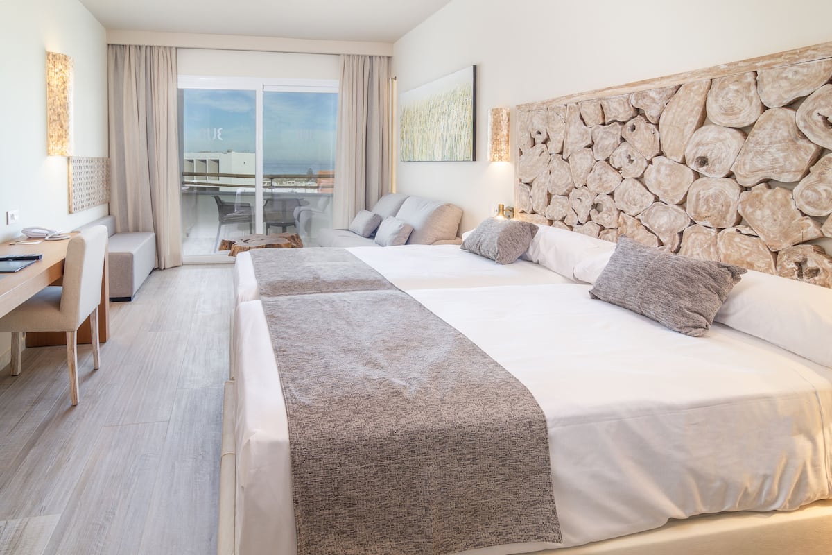 A hotel room with a large bed, a desk, and a view of the sea through the balcony.