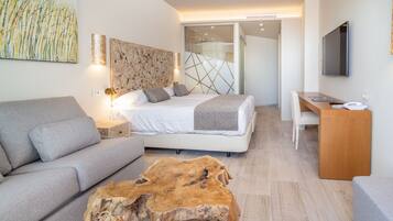 Una habitación de hotel moderna con una cama, un sofá gris, una mesa de centro de madera, un escritorio y un televisor.