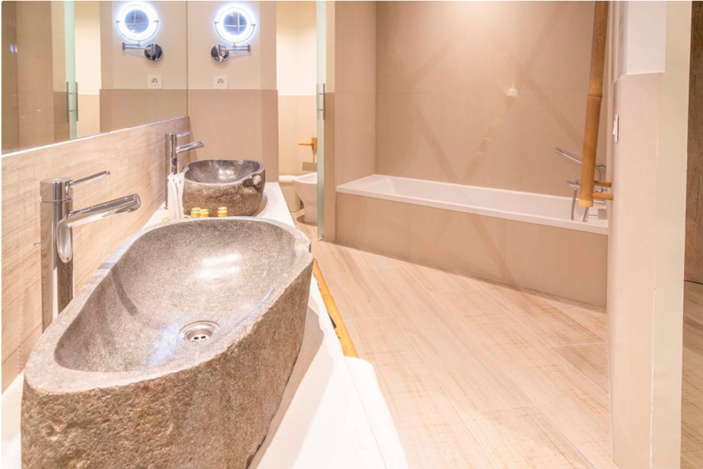 Een badkamer met een grote stenen wasbak, een bad en twee verlichte spiegels.