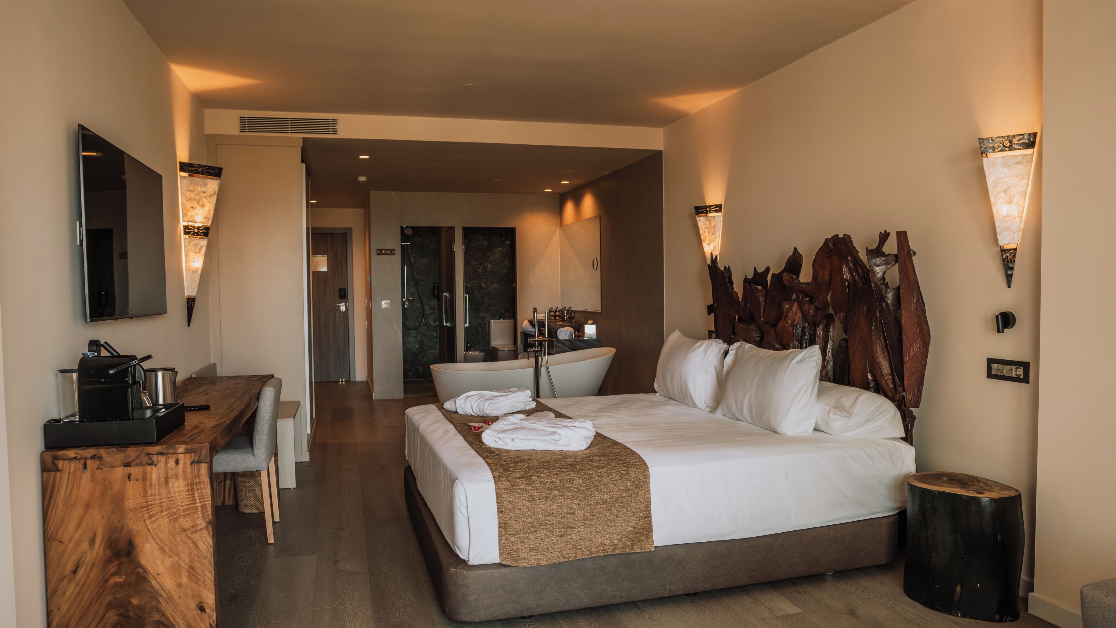 Una habitación de hotel con cama, mesita de noche y escritorio con cafetera.