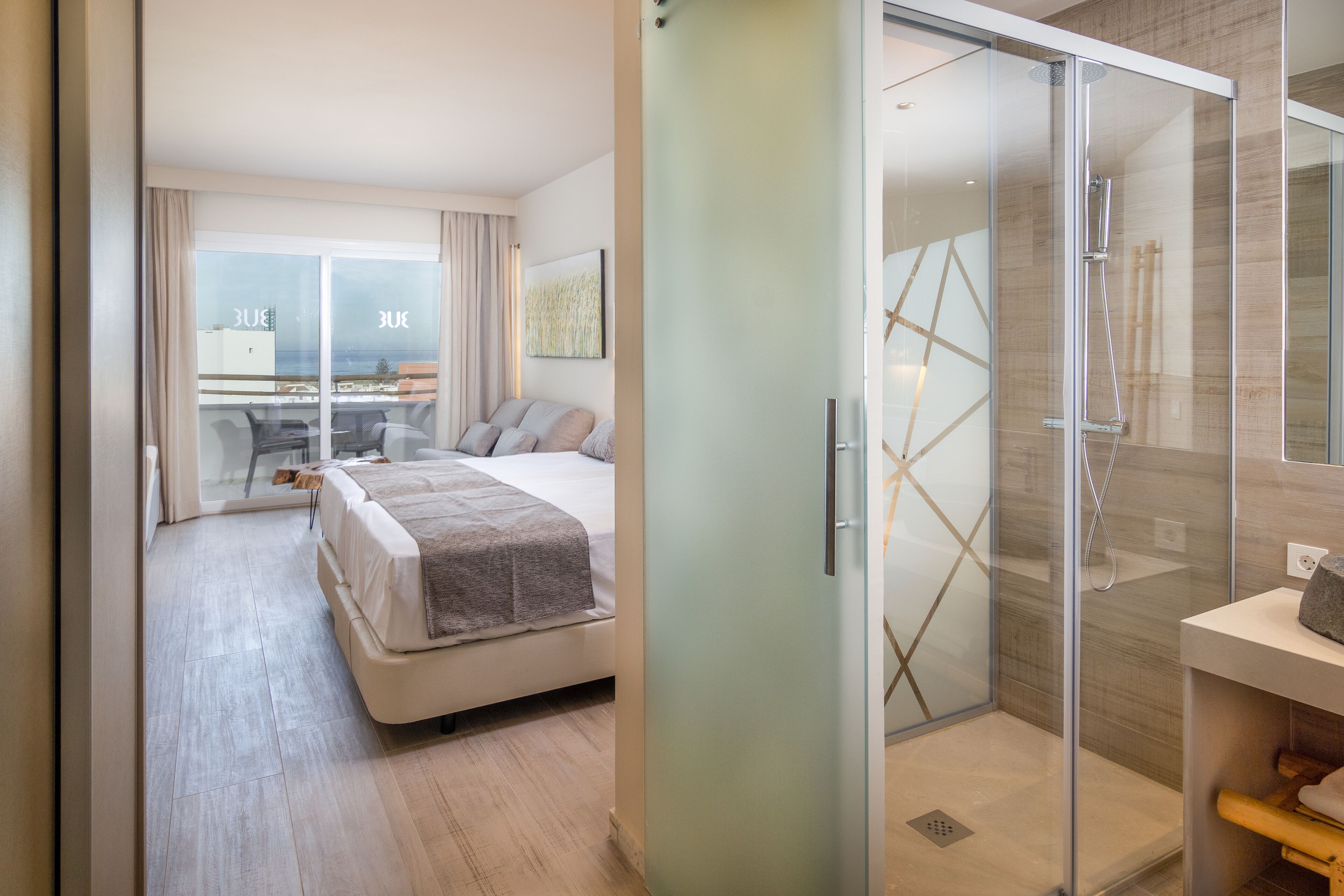 Habitación de hotel moderna con una cama grande, cabina de ducha de vidrio y vistas a la ciudad a través de ventanas de piso a techo.