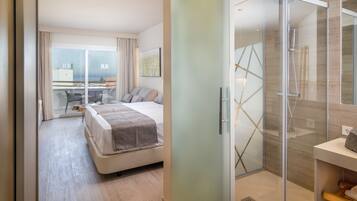 Habitación de hotel moderna con una cama grande, cabina de ducha de vidrio y vistas a la ciudad a través de ventanas de piso a techo.