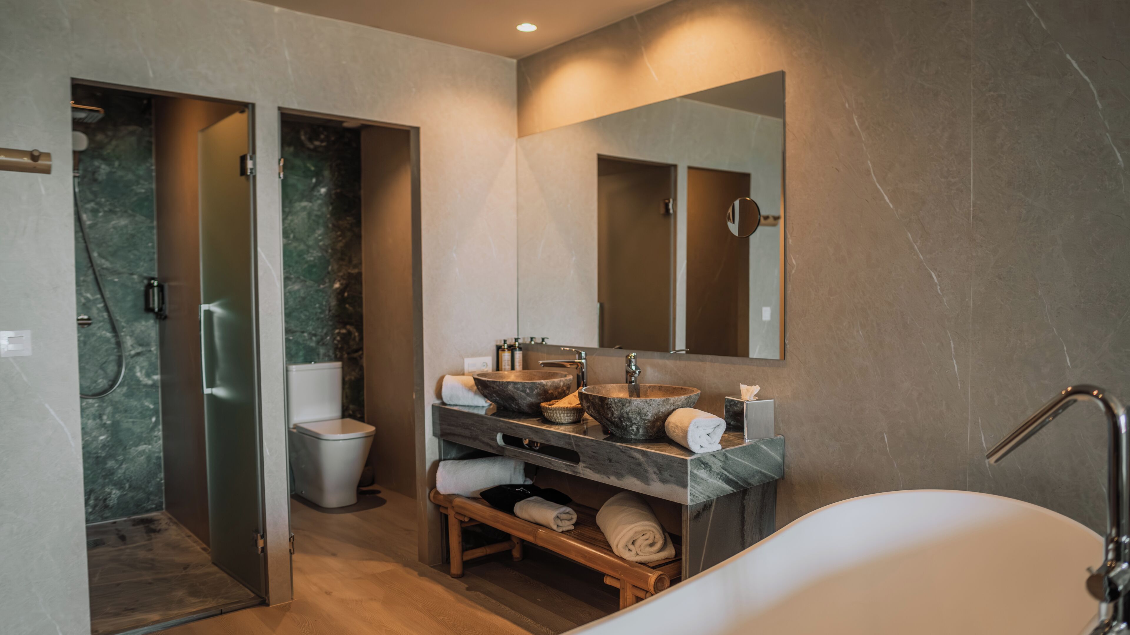 A modern bathroom with a freestanding bathtub, a vanity with two sinks, a large mirror, and a wooden bench.