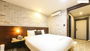Una habitación de hotel con una cama grande, cabecera de madera, mesita de noche con teléfono y lámpara, pared con diseño de ladrillo y unidad de aire acondicionado.