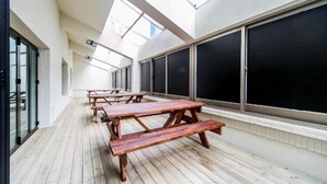 Un espacio al aire libre cubierto con mesas de picnic de madera y ventanas amplias.