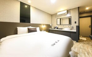 Habitación de hotel con una cama grande, una mesita de noche, un espejo, un lavabo y una puerta.