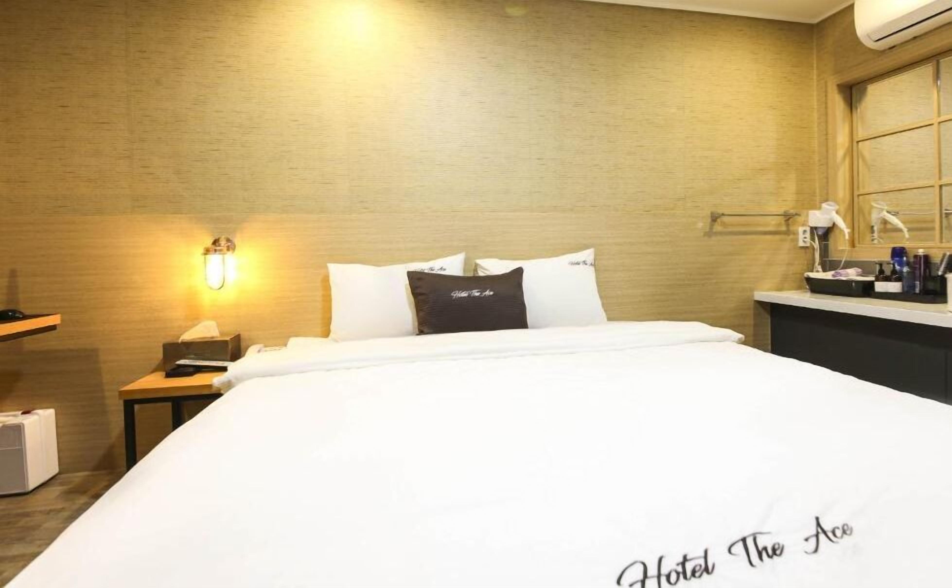 A hotel room with a neatly made bed, a bedside table with a lamp, and a small desk with a telephone.
