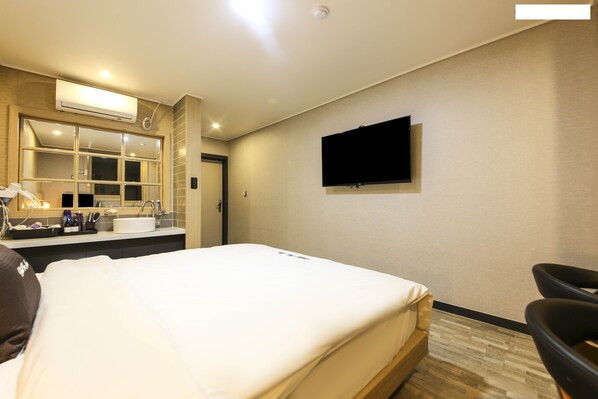 A hotel room with a bed, a TV mounted on the wall, a bathroom with a mirror, sink, and toiletries. - Hotel the Ace (Tongyeong)