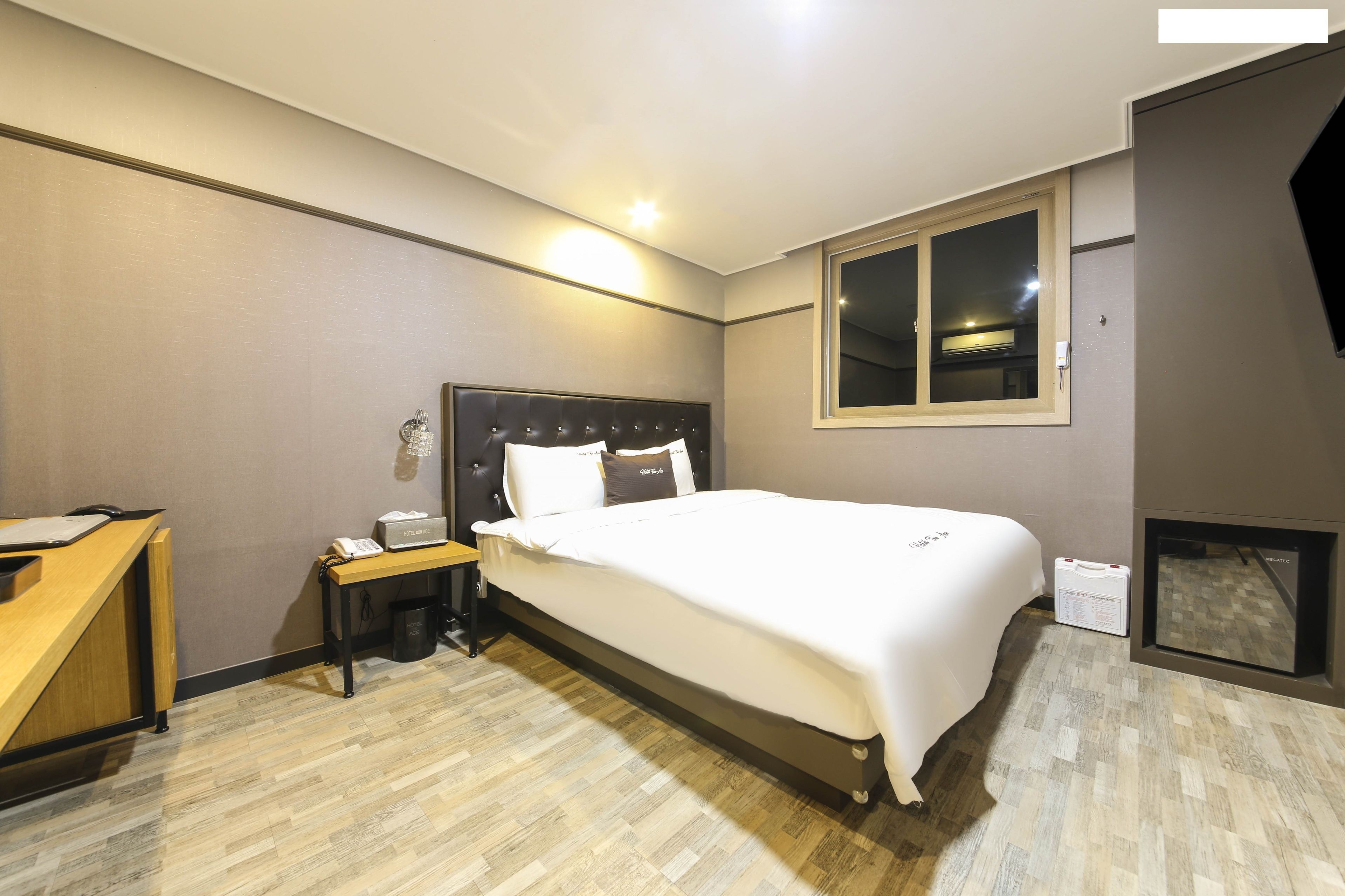 Habitación de hotel con cama, mesita de noche, lámpara y un ventanal.