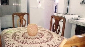 Ein Essbereich mit einem Tisch, bedeckt mit einer gemusterten Tischdecke, zwei hölzernen Stühlen und einer großen Vase.