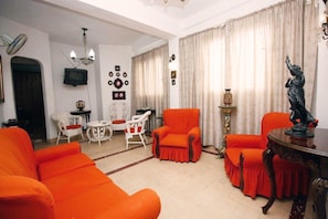 Ein Wohnzimmer mit orangefarbenen Sofas, einem weißen Sessel, einem roten Sessel, einem kleinen runden Tisch und einer Statue.
