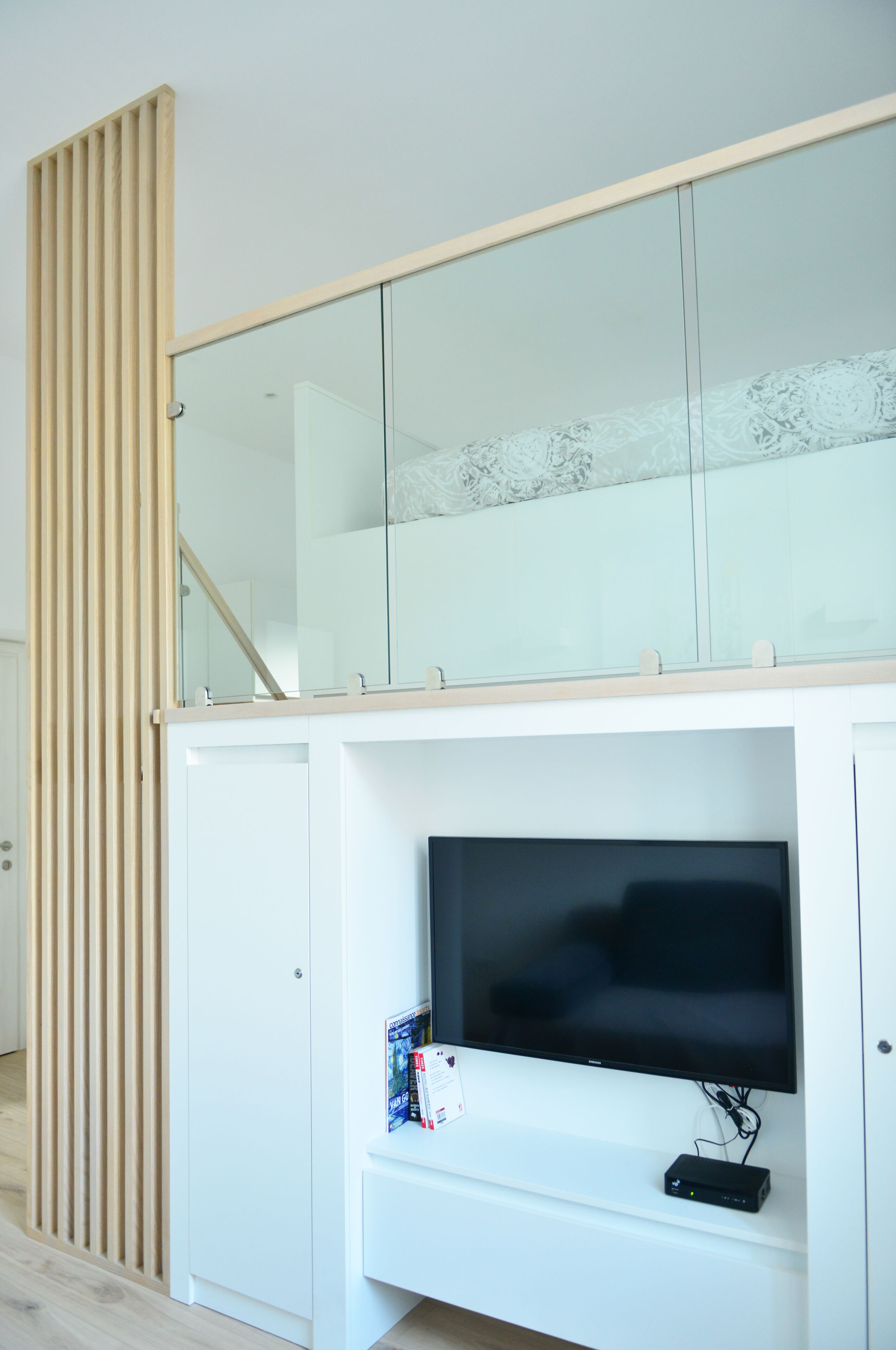 Una sala moderna con un mueble blanco para el equipo multimedia, un televisor de pantalla plana y un separador de listones de madera.