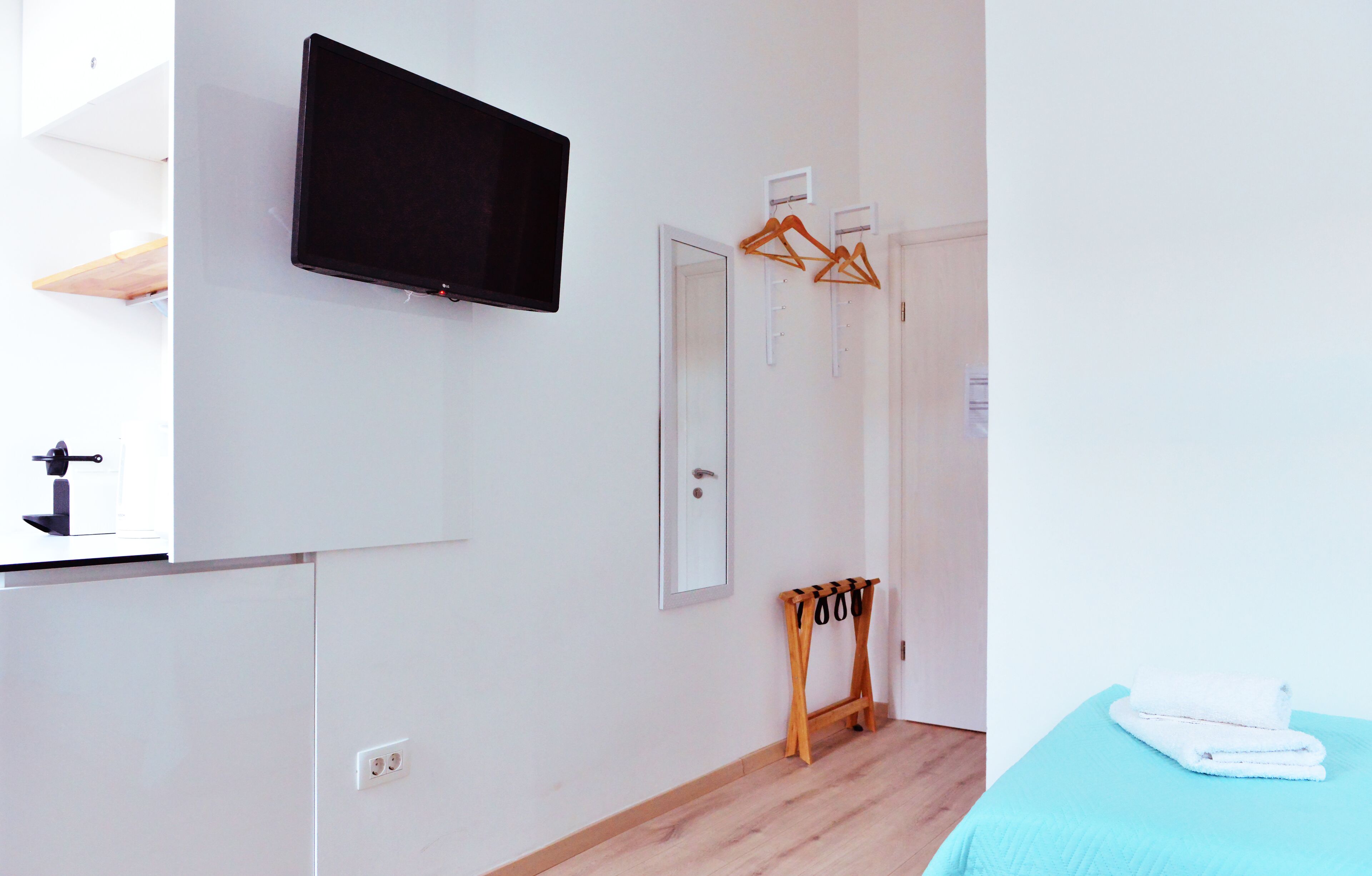 A bedroom with a bed, a TV mounted on the wall, a mirror, and a door with a coat rack.