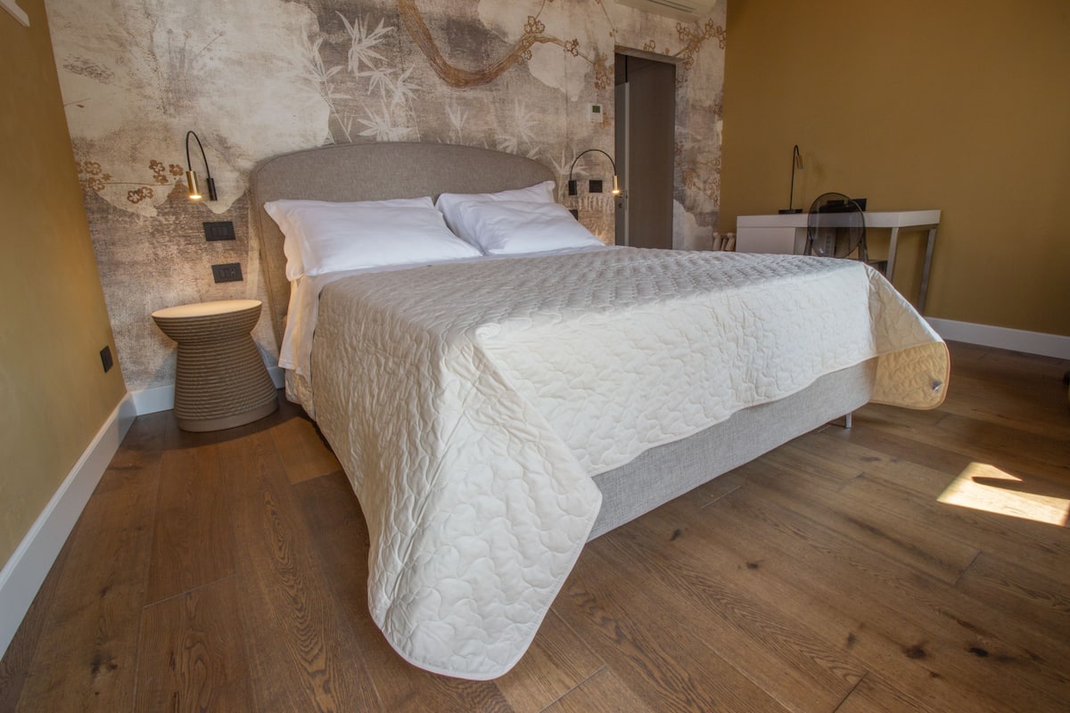 A bedroom with a large bed, a bedside table, a lamp, and a wall-mounted light fixture.