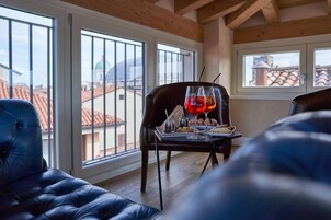 Un coin repas avec une table dressée pour deux personnes, une vue sur les toits à travers de grandes fenêtres et un plafond en bois.