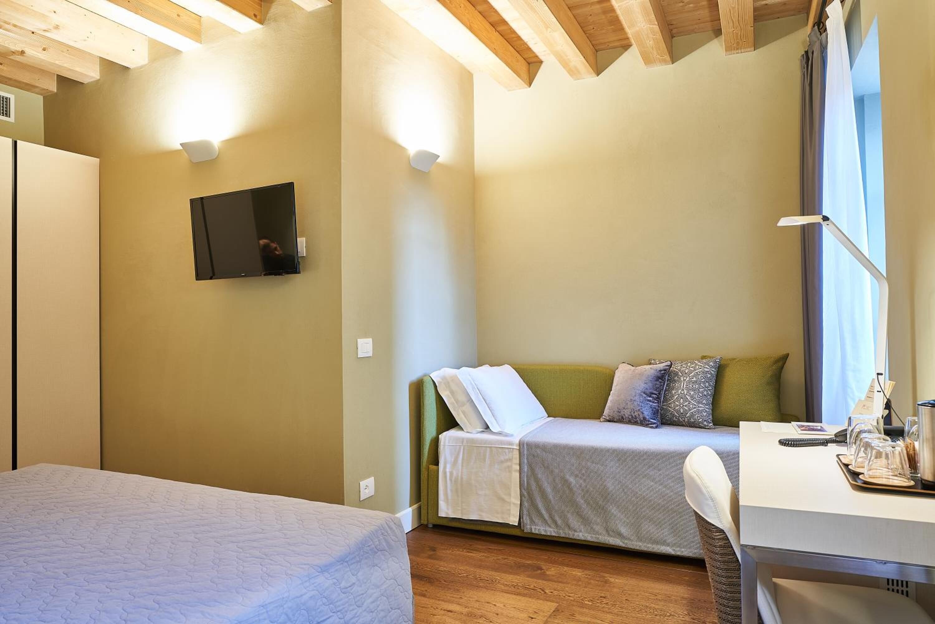 Ein Schlafzimmer mit Bett, einer Couch, einem Schreibtisch und einem an der Wand befestigten Fernseher.
