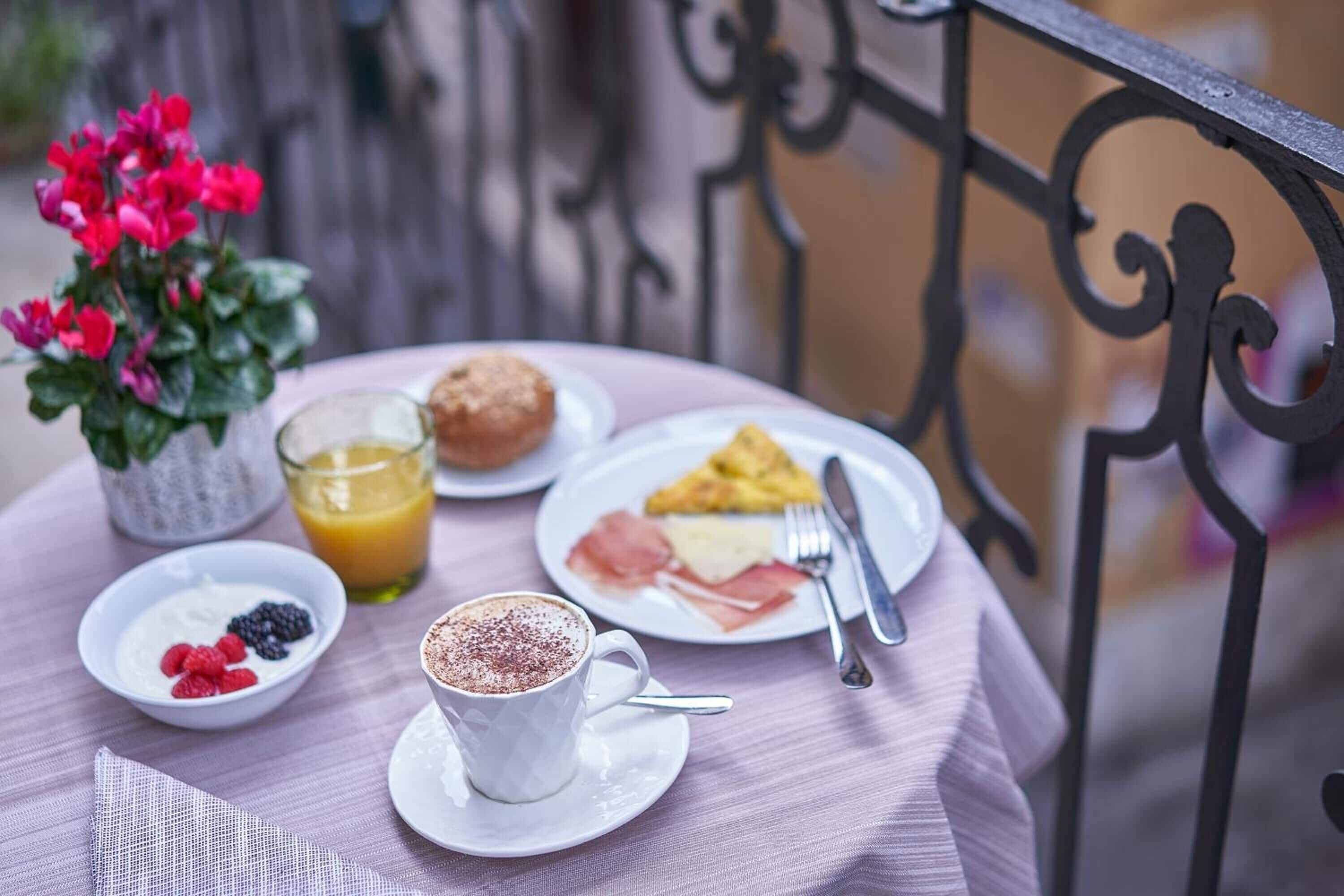 Ein Tisch mit Frühstücksangeboten, darunter eine Tasse Kaffee, ein Glas Orangensaft, ein Teller mit Eiern und Schinken, ein Muffin und eine Schüssel Joghurt mit Beeren.