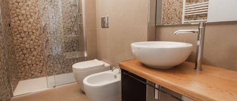 A modern bathroom with a glass shower enclosure, a white sink, and a bidet.