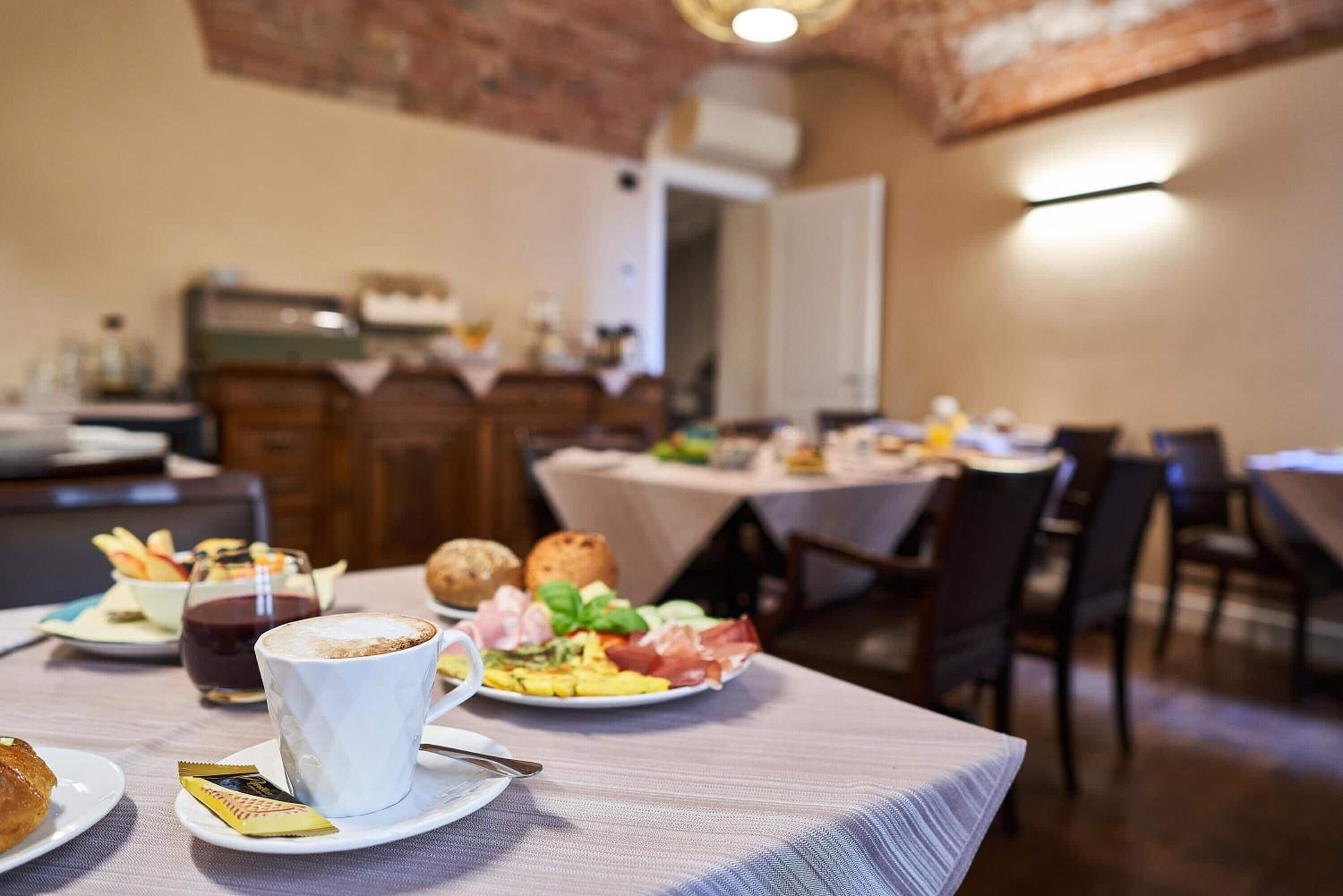 Ein Essbereich mit Tischen, die für das Frühstück gedeckt sind, darunter Teller mit Speisen, eine Tasse Kaffee und ein Glas Saft.