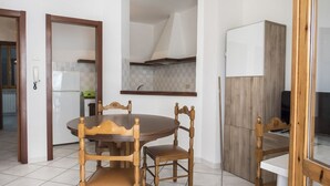 A dining area with a round table and four wooden chairs, a kitchen with a white refrigerator, and a wooden cabinet. - N203 - Numana, large three-room apartment with porch (Numana)
