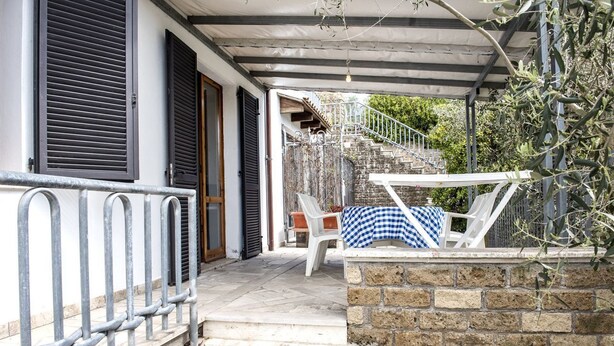 A covered outdoor area with a stone wall, a metal railing, and a staircase leading to a building. - N203 - Numana, large three-room apartment with porch (Numana)