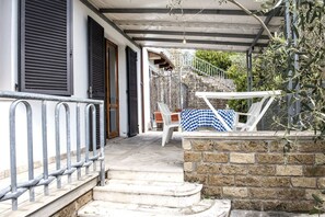 A covered outdoor area with a stone wall, a metal railing, and a staircase leading to a building. - N203 - Numana, large three-room apartment with porch (Numana)