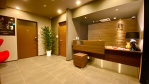 A modern reception area with a wooden reception desk, a potted plant, and a red chair. - Randor Residence Susukino Suites (Sapporo)