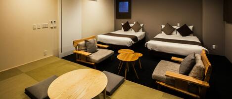 A hotel room with two beds, a small dining table, and a seating area with chairs and ottomans.