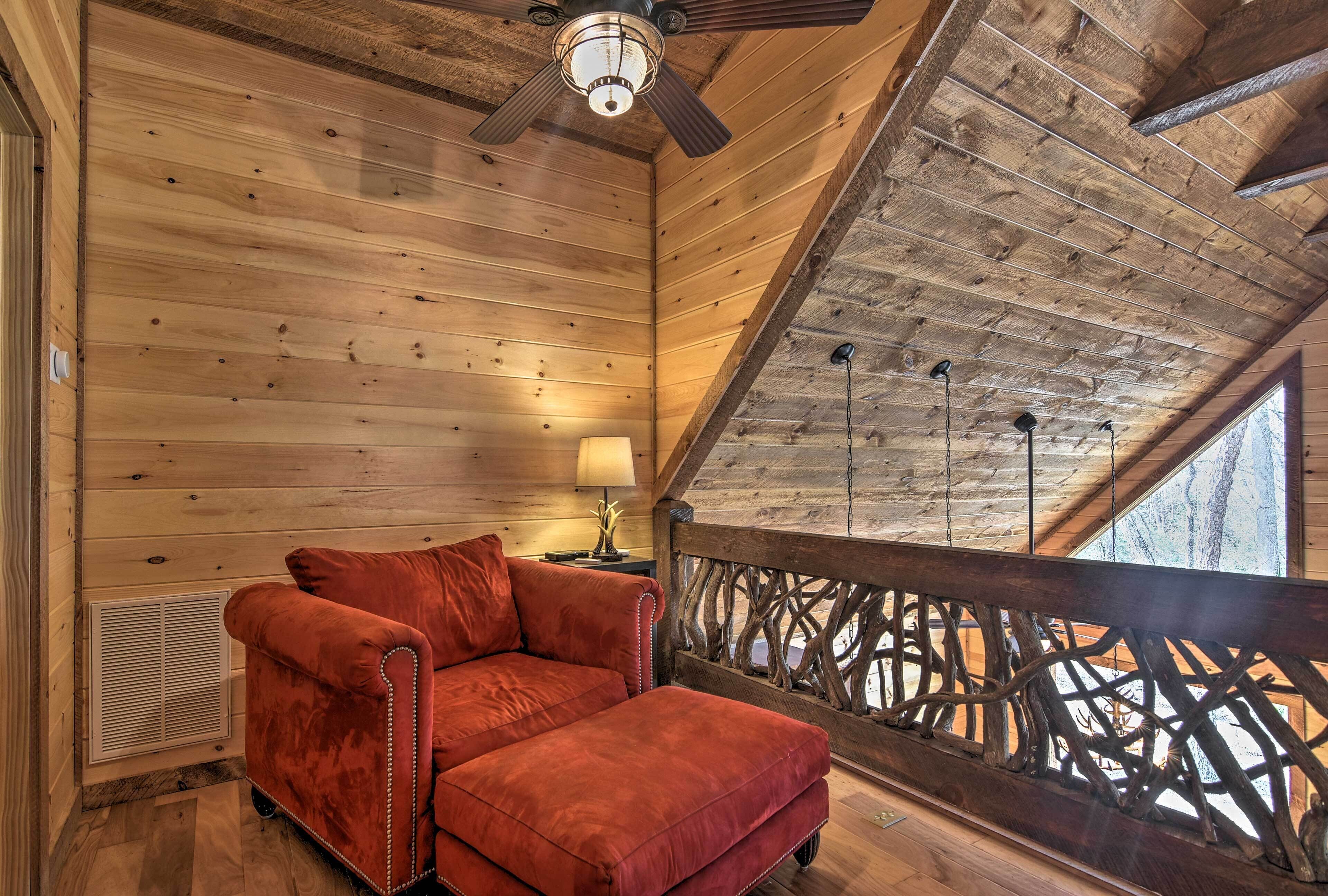 A wooden interior with a red sofa, a ceiling fan, a lamp, and a view through a wooden railing.