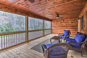 Relax on the porch with a view of the surrounding forest, featuring a comfortable seating area with two chairs and a table.