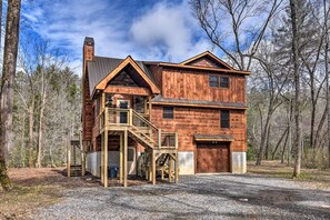 Situated in a wooded area, this cabin features a front deck and a garage with a staircase leading to an upper level.
