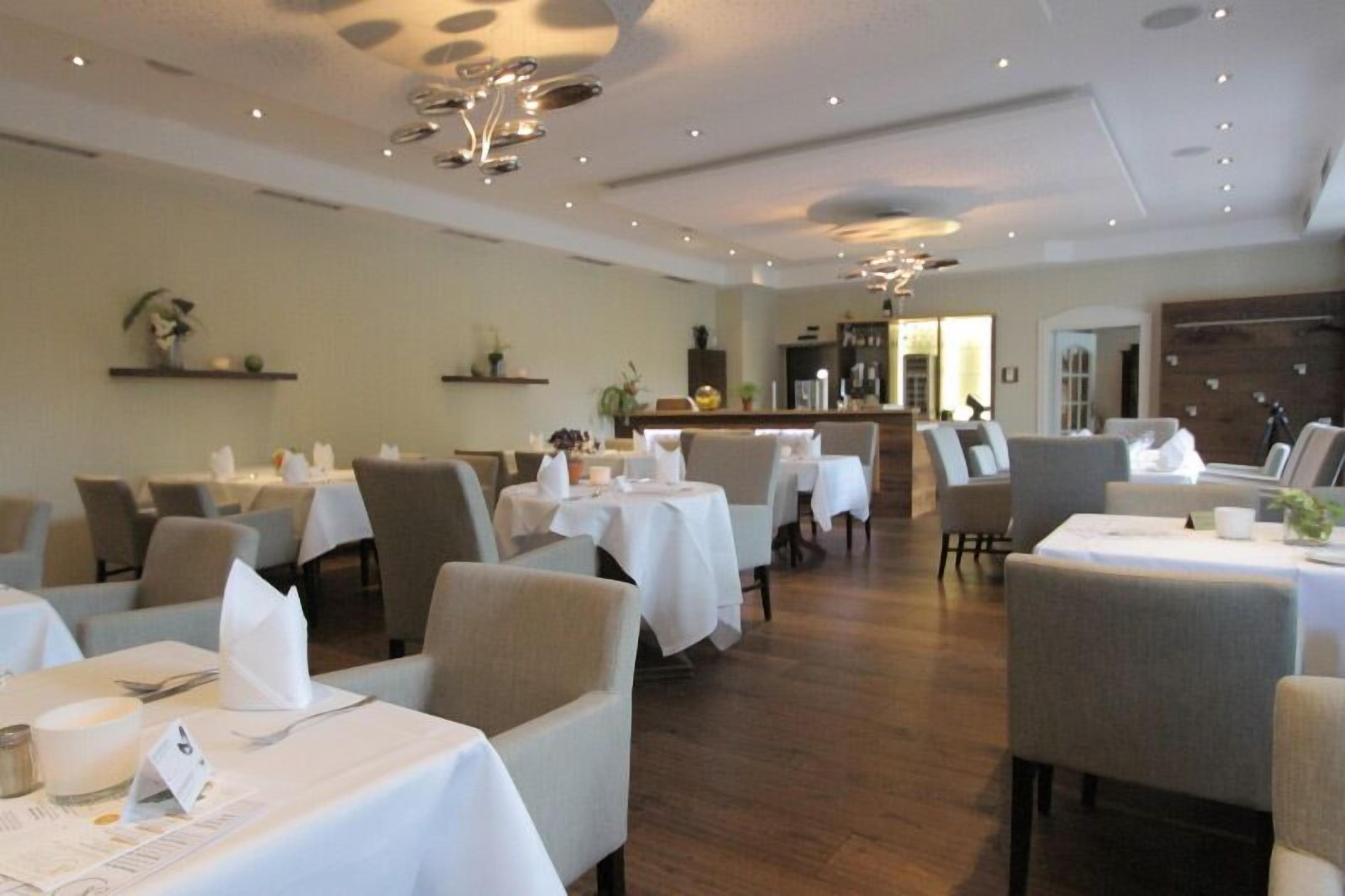 Un restaurante con varias mesas y sillas, manteles blancos y suelo de madera.