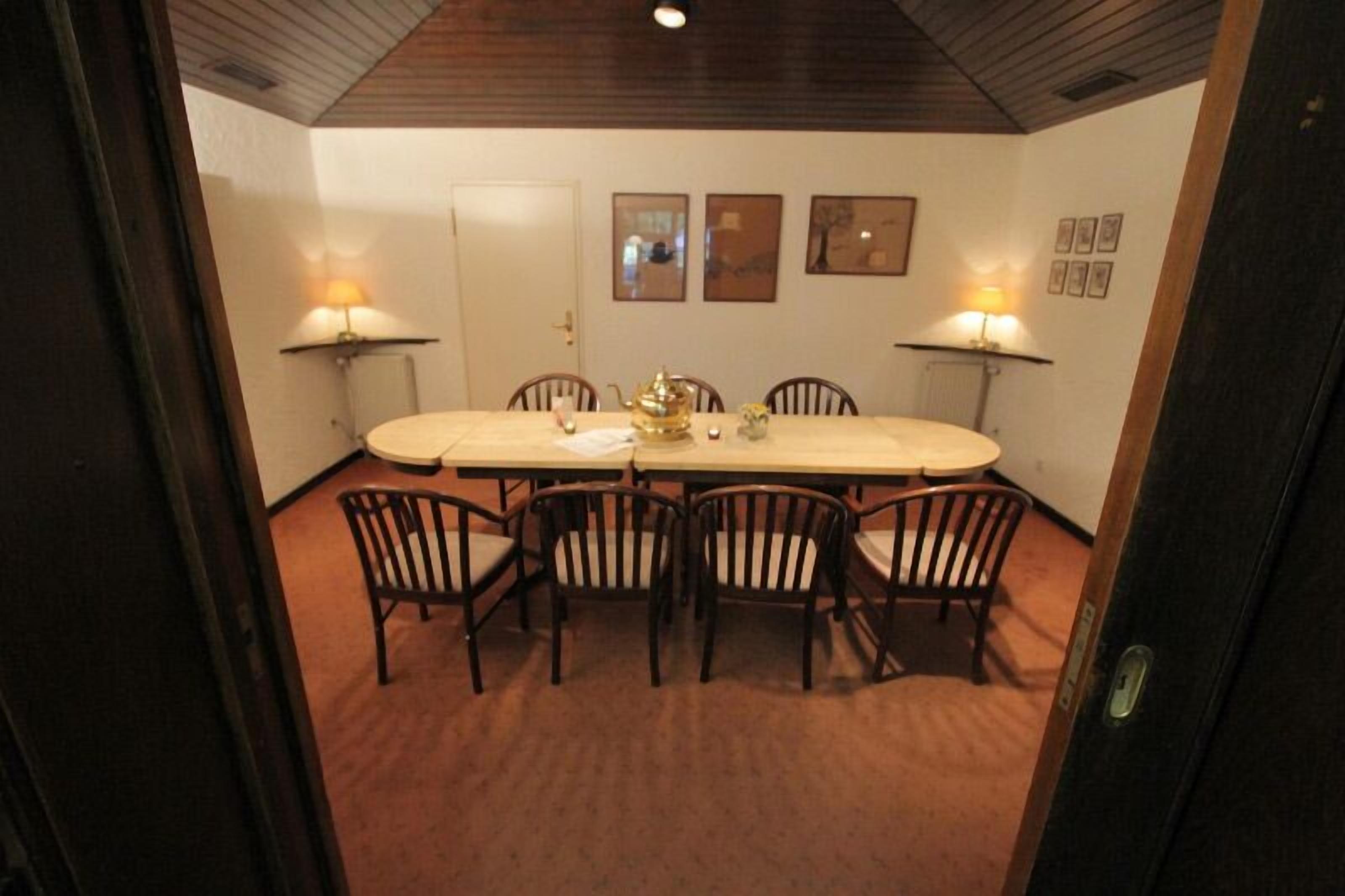 A dining room with a round table, six chairs, two wall-mounted lamps, and framed pictures on the wall.